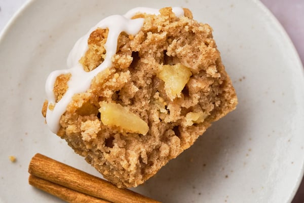 A vegan apple muffin, cut in half, on a plate with a cinnamon stick. 