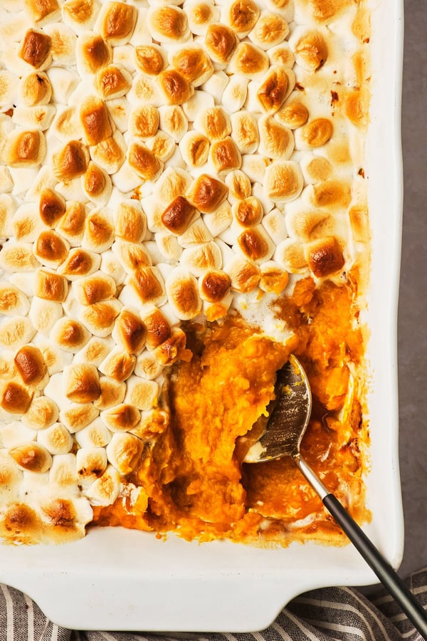 A top-down view of a vegan sweet potato casserole topped with marshmallows, with a serving spoon in the corner of the dish.