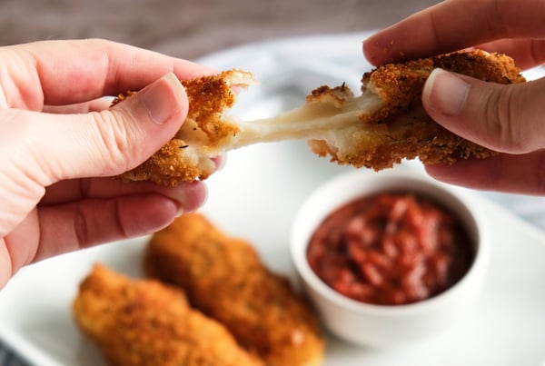 Two hands breaking apart a stretchy vegan mozzarella stick