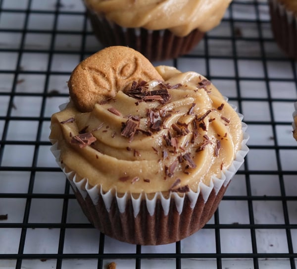 A closeup of a chocolate cupcake with cookie butter frosting, topped with shaved chocolate and a speculoos cookie