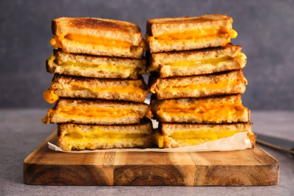 Five different grilled cheeses with five vegan cheeses, stacked on a serving board