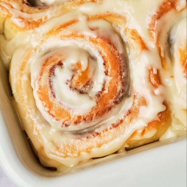 Vegan cinnamon rolls in a casserole dish, topped with vegan cream cheese frosting.