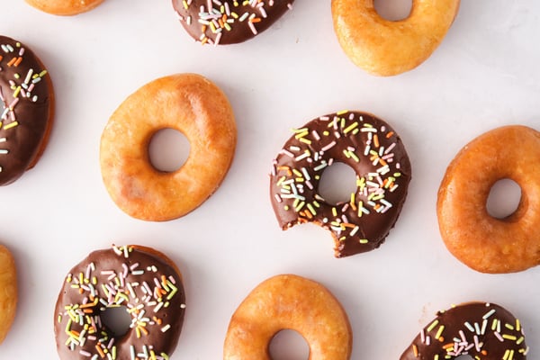 A top-down view of vegan chocolate frosted and glazed donuts, with one bitten.