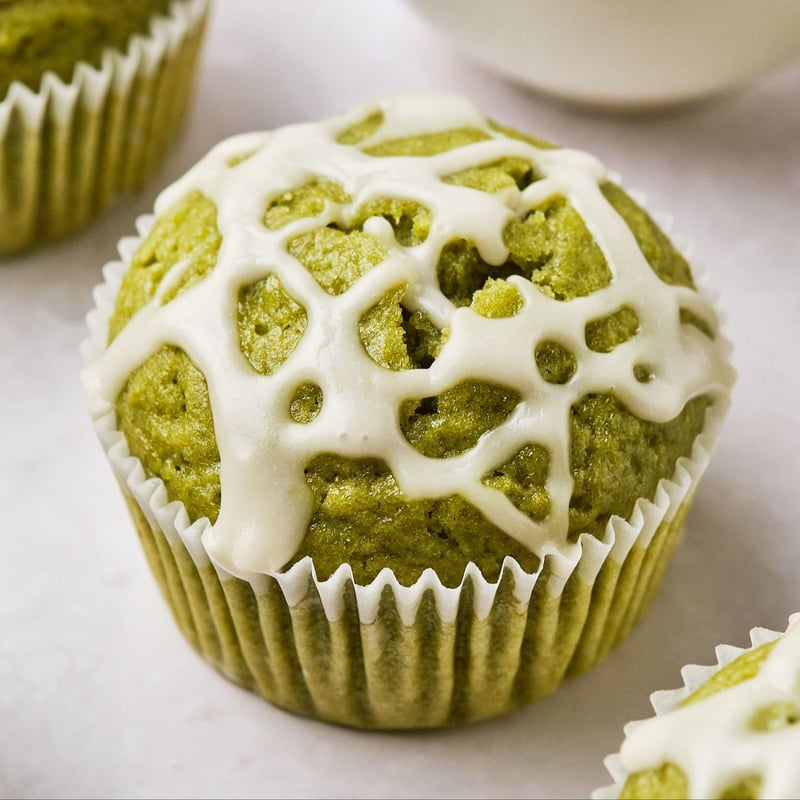 A close-up view of a vegan matcha muffin, topped with a vanilla icing drizzle. 