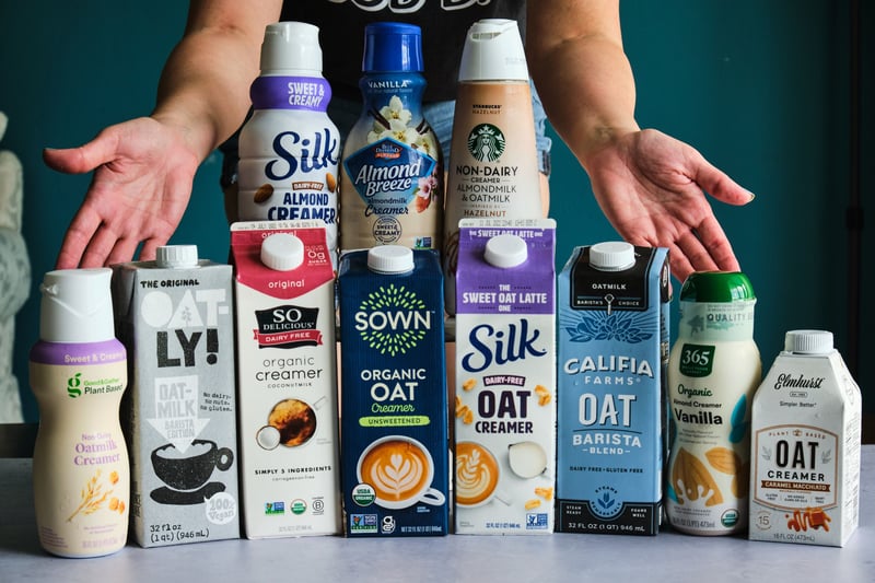 Eleven vegan creamers lined up on a table, with hands behind them.