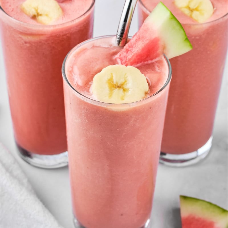 A watermelon banana smoothie in a glass with a straw, garnished with a slice of watermelon and banana.