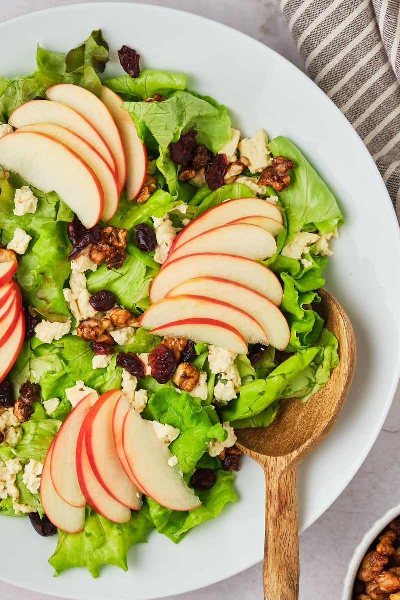 Close-up view of apple walnut salad in a bowl with a serving spoon.