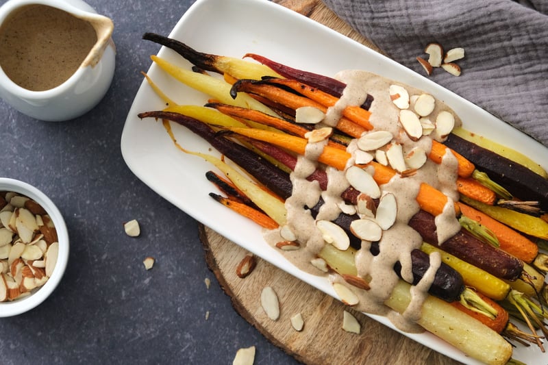 Roasted carrots on a platter with a cashew-tahini sauce and almond slices to the side
