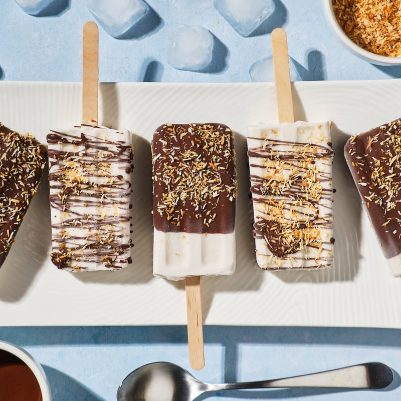Coconut popsicles with a chocolate coating and toasted coconut shreds on a platter.