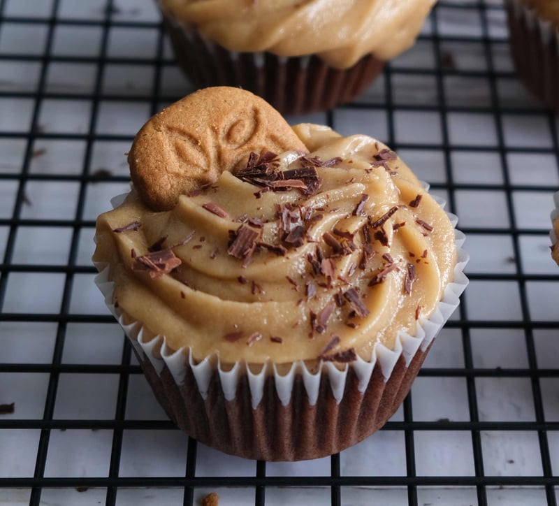 A closeup of a chocolate cupcake with cookie butter frosting, topped with shaved chocolate and a speculoos cookie
