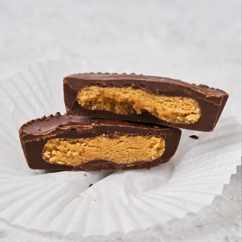 A vegan peanut butter cup on an open wrapper, cut in half and stacked to show the peanut butter filling inside. 