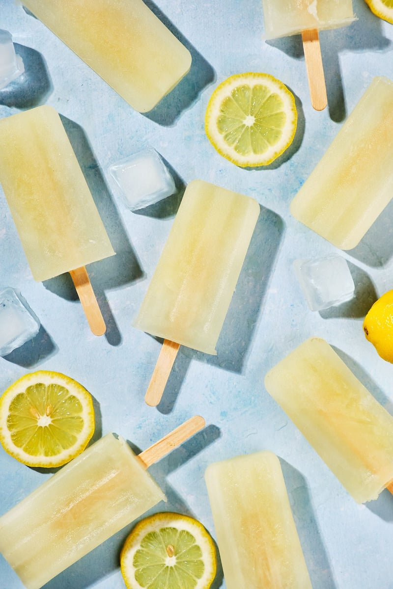 Lemonade popsicles, lemon slices, and ice cubes on a table. 