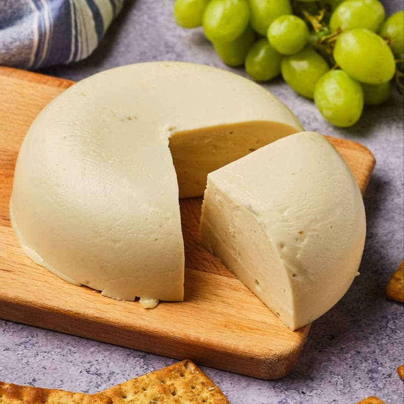 Vegan Gruyere cheese on a wooden board surrounded by grapes and crackers. 