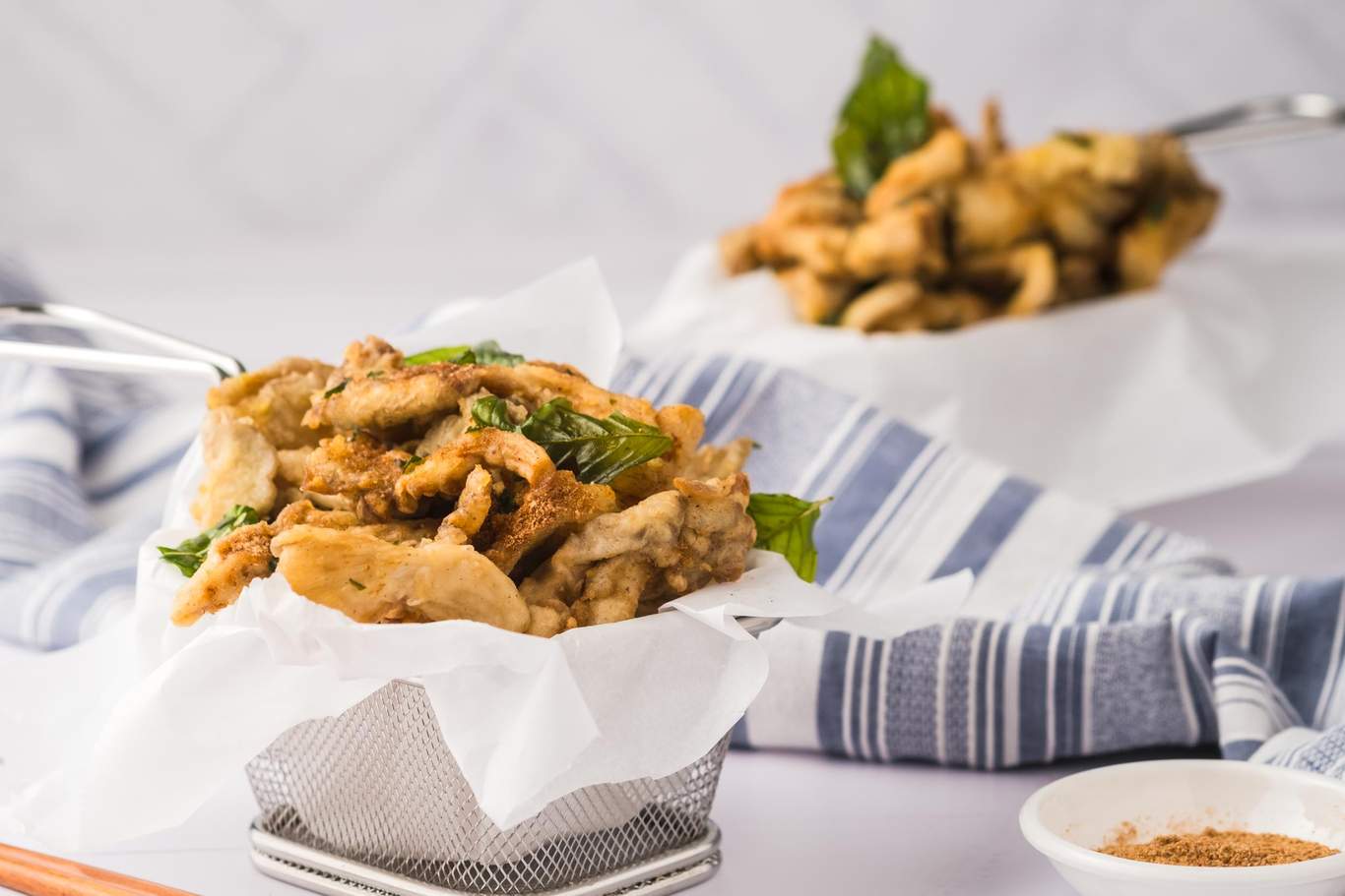 Two baskets of fried oyster mushrooms, with a bowl of seasoning powder to the side.