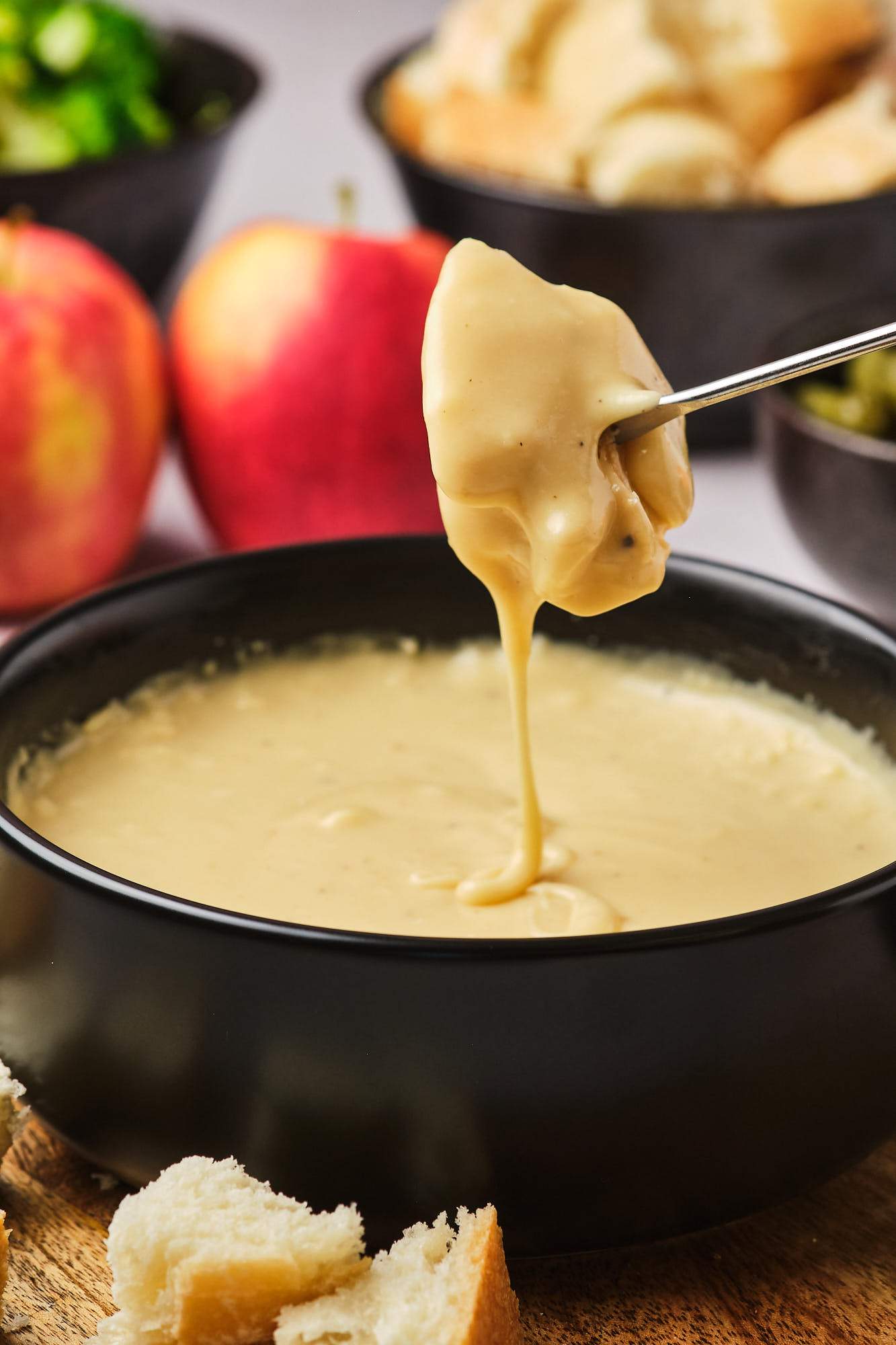 A fondue fork holding a dipped piece of bread over the pot of vegan fondue as the cheese drips into the pot. 