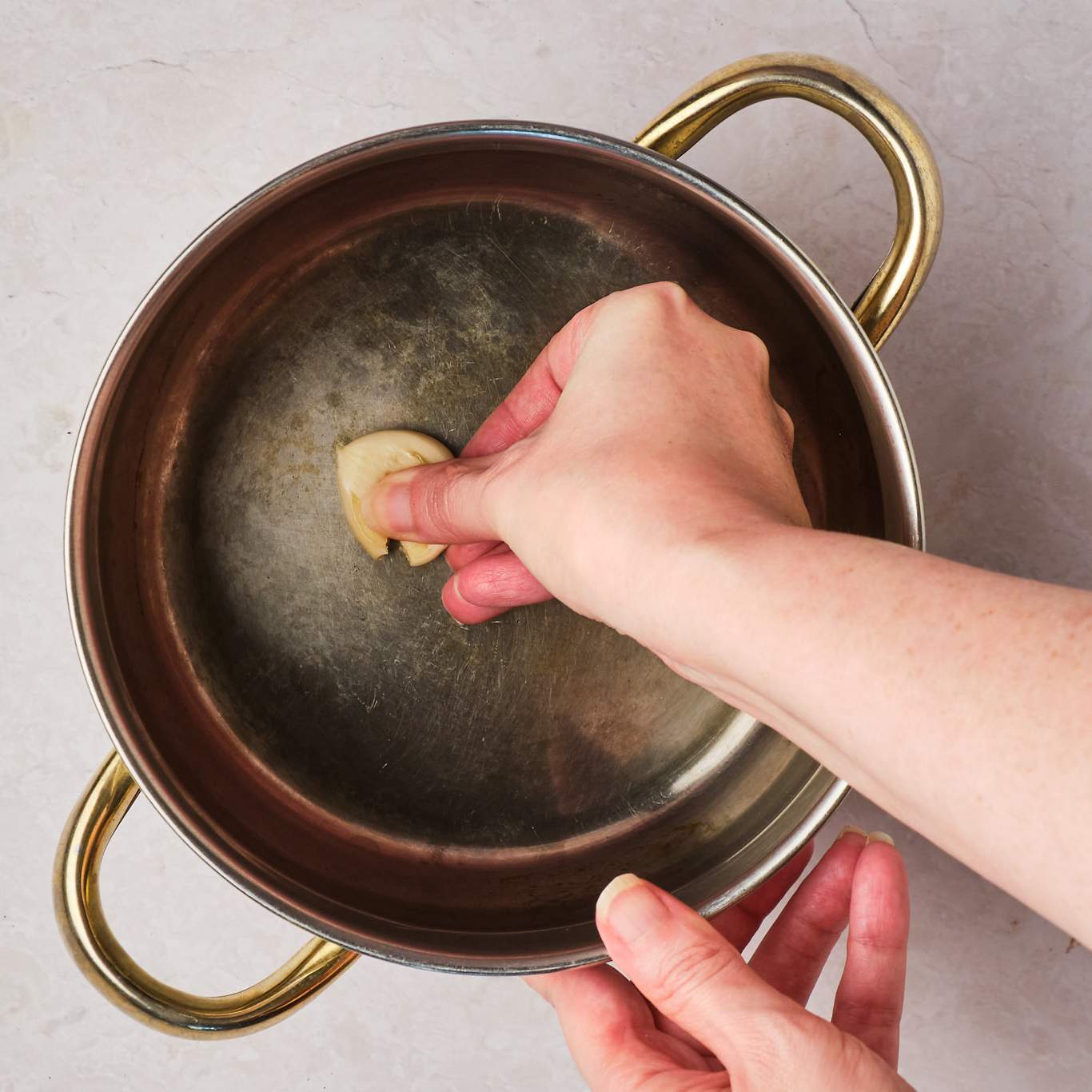 A hand rubbing a clove of garlic inside a pot. 